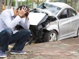 Man holding his head next to the scene of a car accident