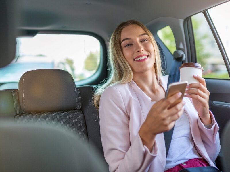 Photo of a woman holding her cell phone while riding in the backseat of an Uber rideshare vehicle