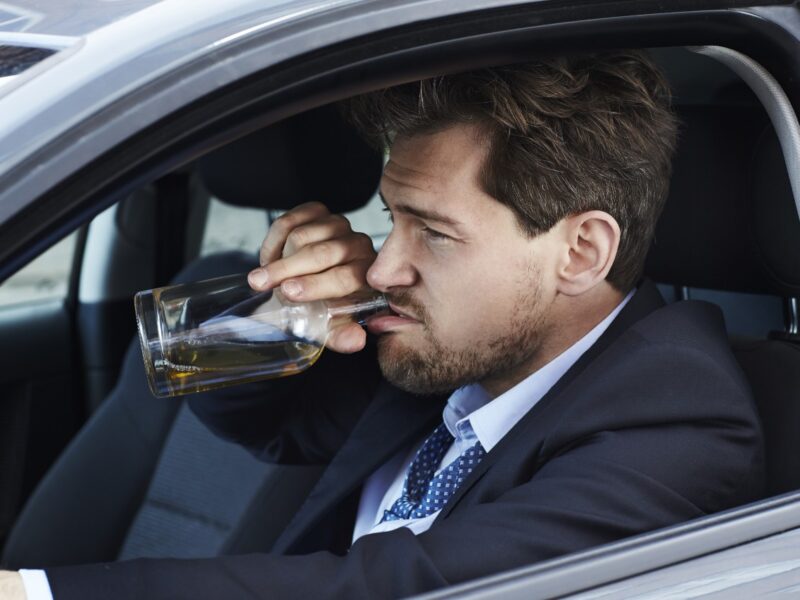 Photo if a businessman drinking alcohol while driving a car