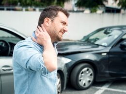 photo of a man holding his neck in pain at the scene of a car accident