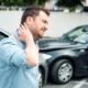 photo of a man holding his neck in pain at the scene of a car accident