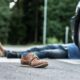 Person lying on a road with one brown shoe in the foreground and a car wheel visible to the right, suggesting an accident scene.